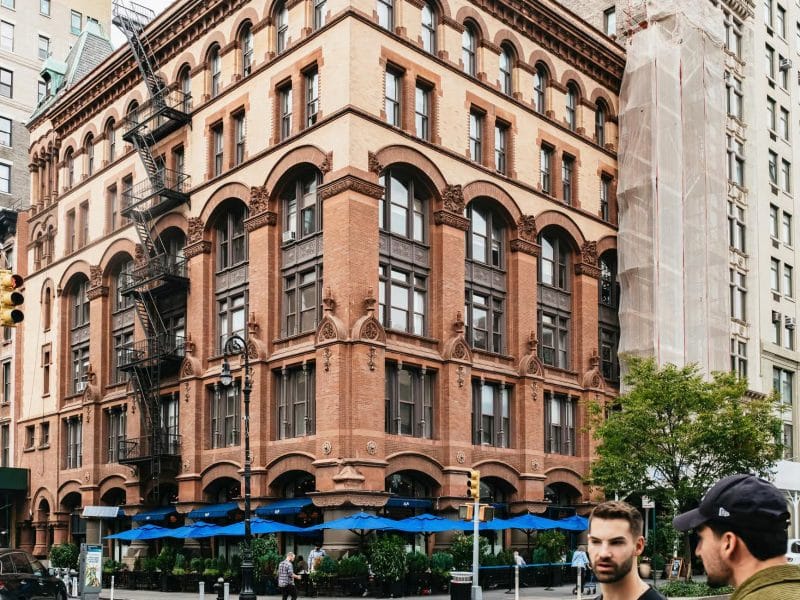 Historic building in downtown NYC, featuring intricate architectural details, surrounded by pedestrians, with outdoor seating under blue umbrellas, relevant to Taylor Swift hotspots tour.