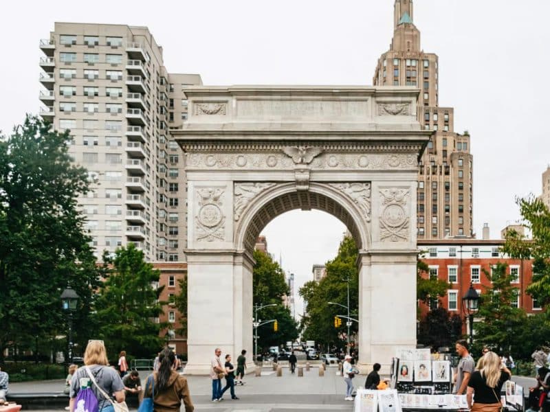 Washington Square Arch in New York City, surrounded by trees and people, symbolizing a vibrant urban atmosphere related to Taylor Swift's NYC hotspots tour.