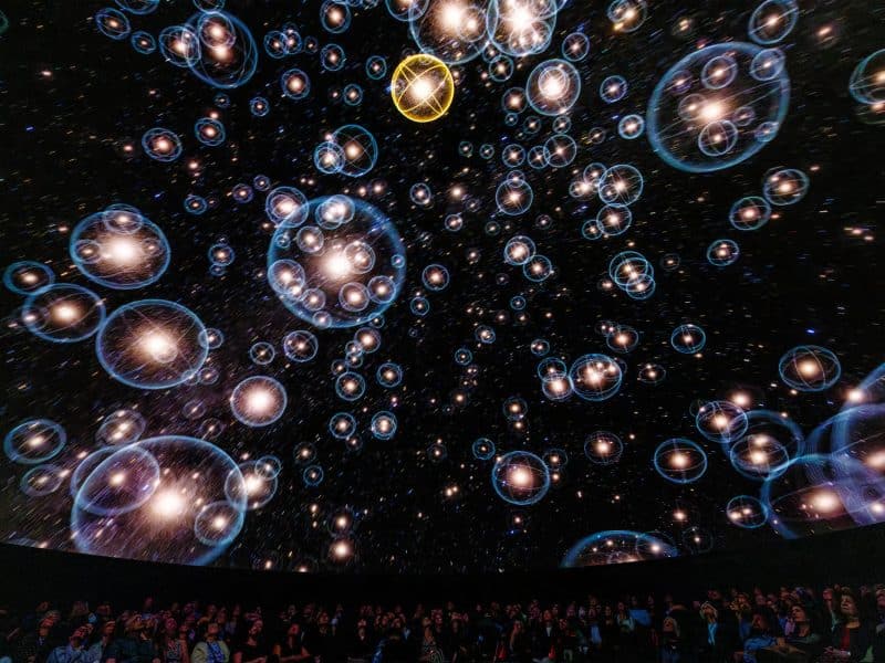 Immersive planetarium experience at the American Museum of Natural History with a starry night sky, glowing celestial bodies, and an audience captivated by the cosmic display.