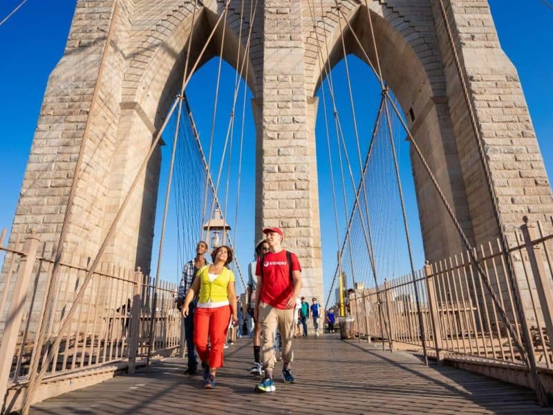 People walking on the Brooklyn Bridge, enjoying views of Manhattan and Brooklyn, part of a food tour in Brooklyn Heights and DUMBO.