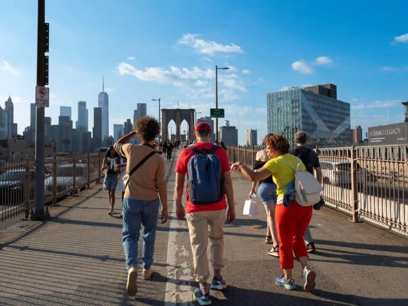 Group of people walking on Brooklyn Bridge with views of Manhattan skyline, enjoying a food tour experience in Brooklyn Heights and DUMBO.