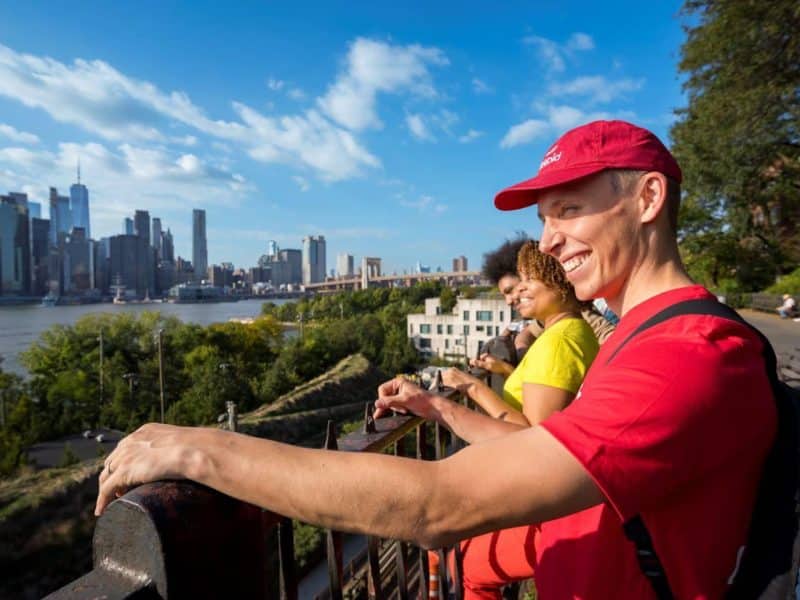 Group of people enjoying views of Manhattan and the Brooklyn Bridge from Brooklyn Heights, highlighting the scenic backdrop of the Hudson River and city skyline during a food tour.