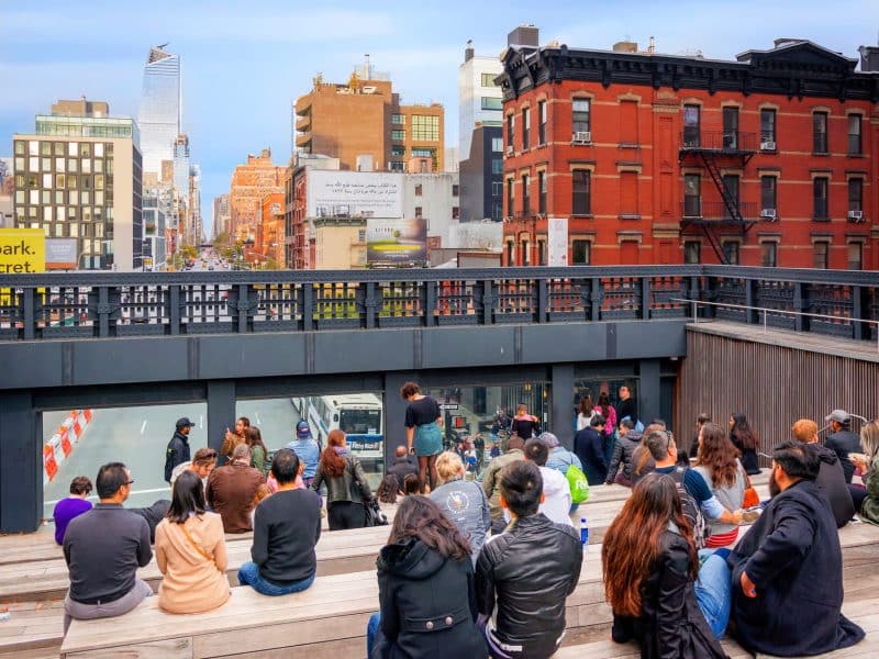 People seated on a wooden platform overlooking the High Line in New York City, with views of the Meatpacking District and surrounding buildings, capturing the vibrant atmosphere of a culinary tour.