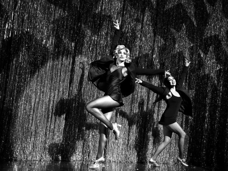 Dancers performing in "Chicago" on Broadway, showcasing iconic choreography against a shimmering backdrop.