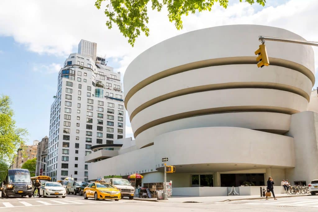 Guggenheim Museum exterior with unique spiral architecture, surrounded by city buildings and traffic, showcasing its significance as a modern art landmark in New York.