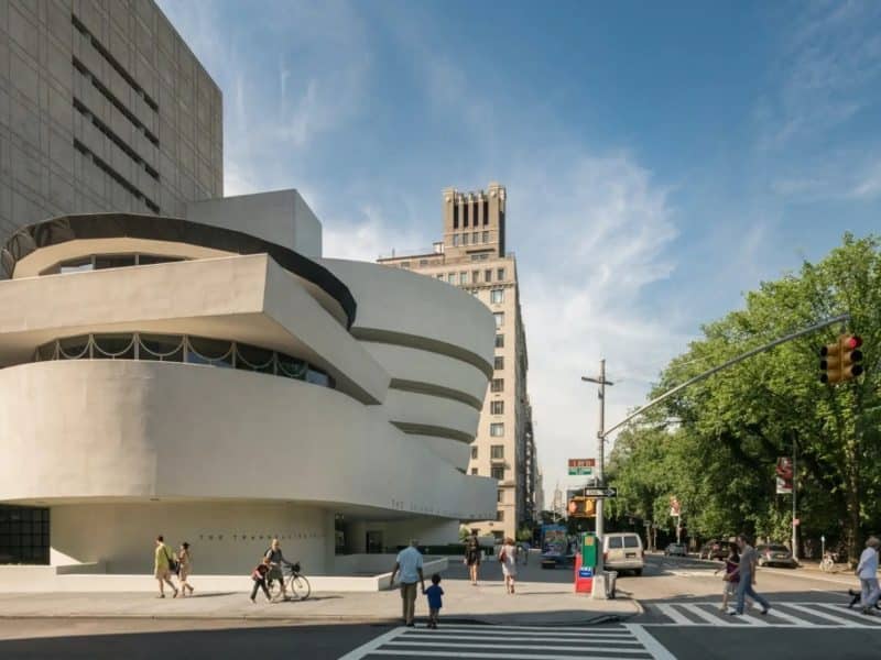 Guggenheim Museum exterior featuring Frank Lloyd Wright's iconic spiral design, surrounded by pedestrians and urban landscape, emphasizing its status as a landmark for modern art and UNESCO World Heritage Site.
