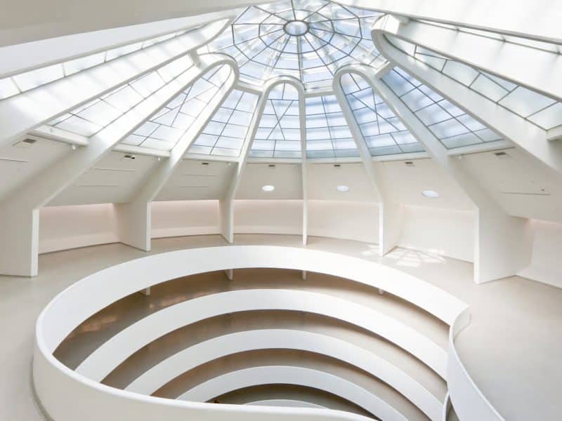 Interior view of the Solomon R. Guggenheim Museum, featuring Frank Lloyd Wright's iconic spiral ramp and a glass dome ceiling, emphasizing its architectural significance as a UNESCO World Heritage Site.