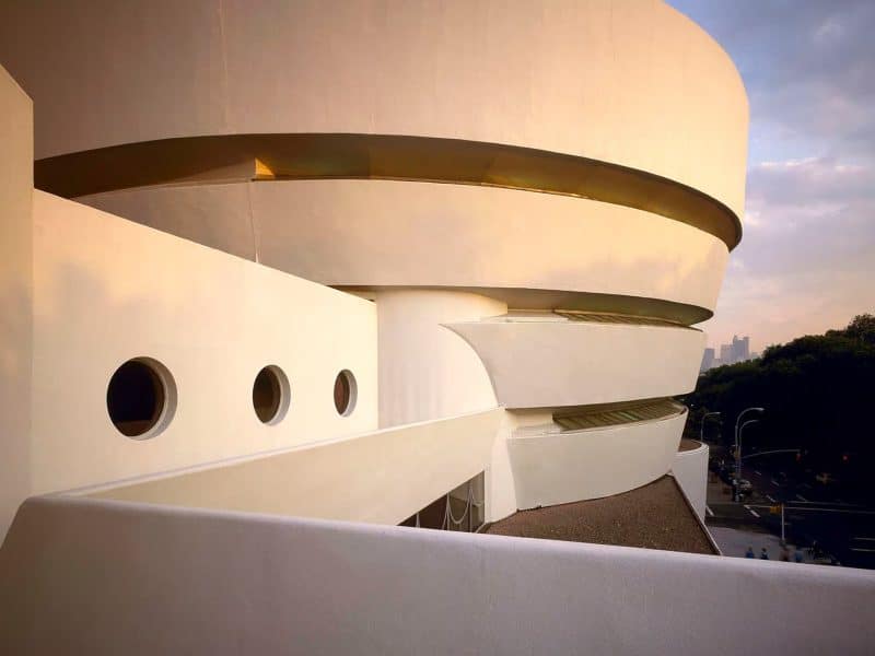 Guggenheim Museum exterior featuring Frank Lloyd Wright's iconic spiral architecture, showcasing modern design elements and circular windows against a city backdrop.