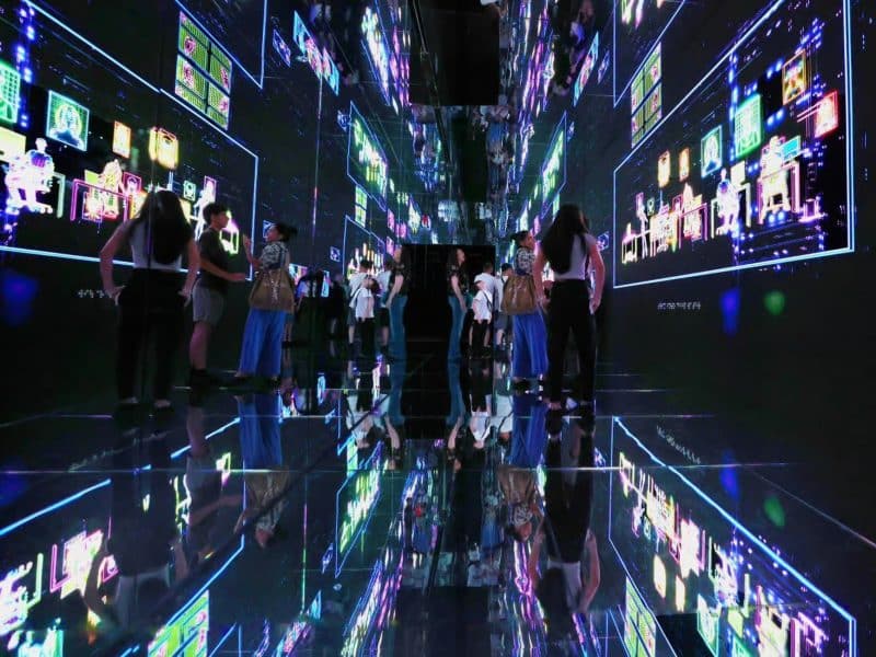 Visitors interacting with immersive digital displays in a reflective corridor at Mercer Labs Museum of Art and Technology, showcasing vibrant art and technology integration.