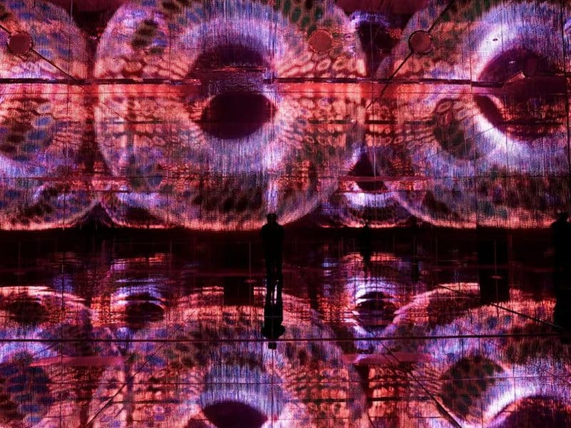 Person standing in front of a vibrant, immersive digital art installation with swirling patterns and reflections, showcasing the innovative technology featured at Mercer Labs Museum of Art and Technology.