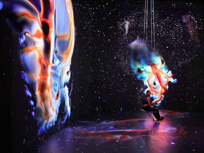 Interactive immersive experience at Mercer Labs Museum of Art and Technology, featuring a person on a swing surrounded by vibrant, colorful digital projections in a starry environment.