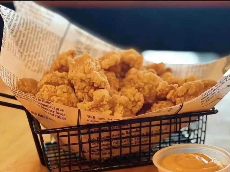 Crispy fried chicken pieces in a basket lined with newspaper, accompanied by a small cup of dipping sauce, showcasing Flushing's vibrant culinary scene.