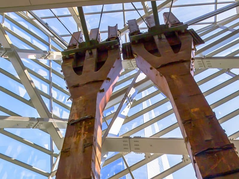 Twin steel beams of the 9/11 Memorial Museum beneath a glass ceiling, symbolizing resilience and remembrance.