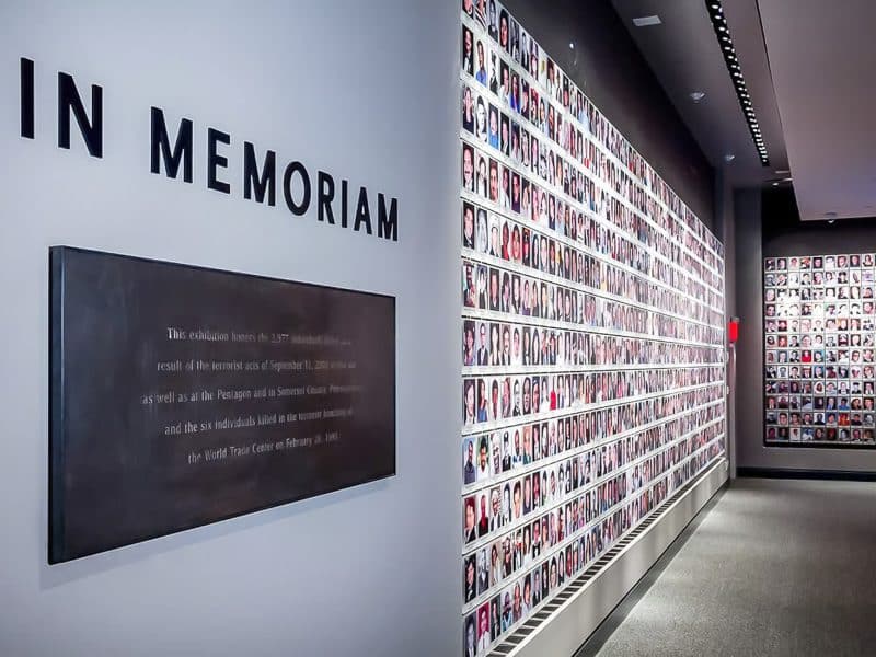 In Memoriam exhibit at the 9/11 Memorial Museum, featuring a wall of photographs honoring victims of the September 11 attacks, with a plaque detailing the exhibition's significance.