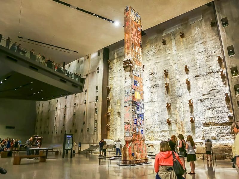 Interior of the National September 11 Memorial Museum featuring the Last Column, surrounded by visitors and the textured concrete wall, symbolizing resilience and remembrance.