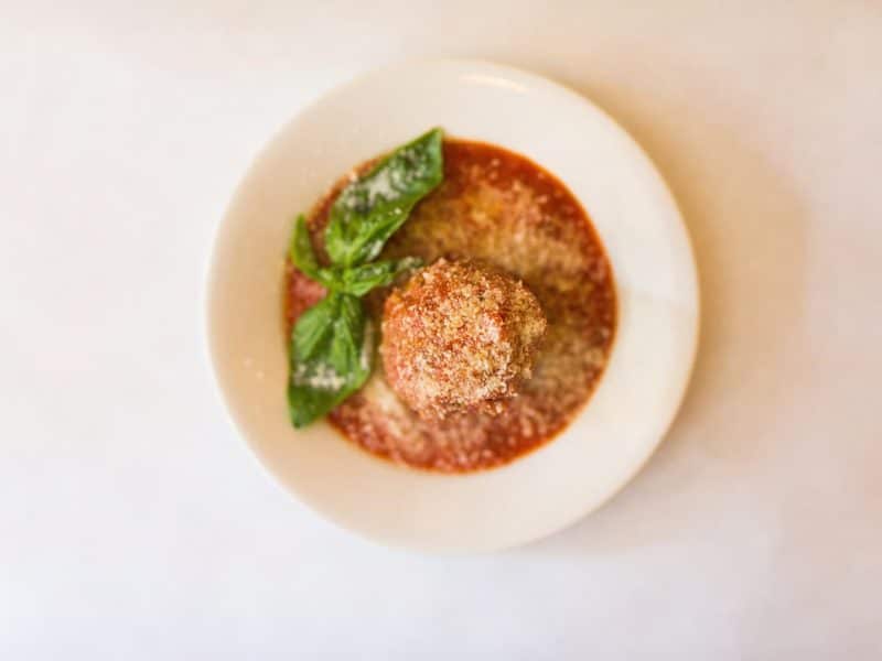 Plate of meatball topped with grated cheese and fresh basil in marinara sauce, representing the culinary delights of the Original Greenwich Village Food & Culture Walking Tour.