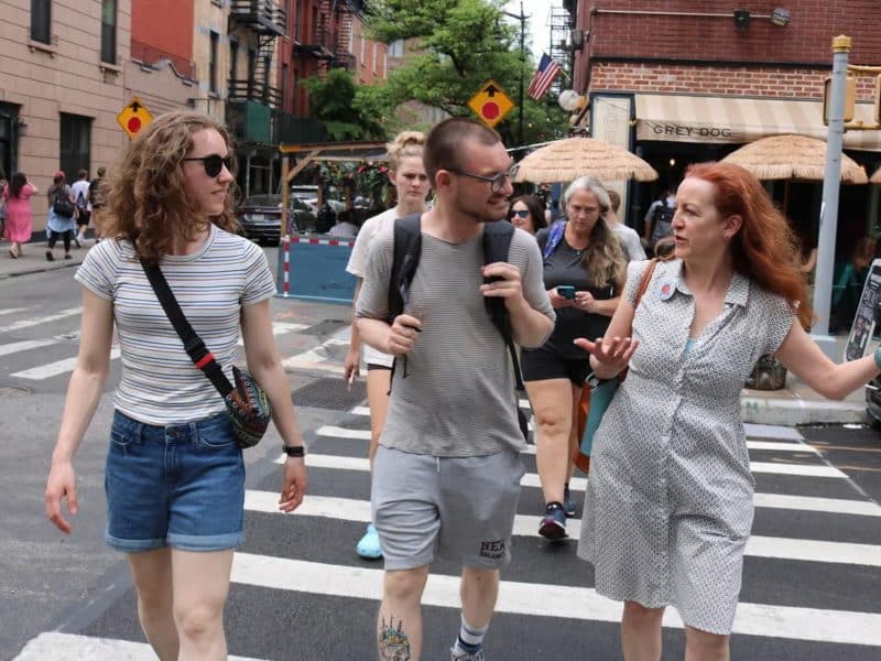 Group of diverse individuals walking in Greenwich Village, engaging in conversation, with a cozy café in the background, representing the vibrant food culture of NYC.