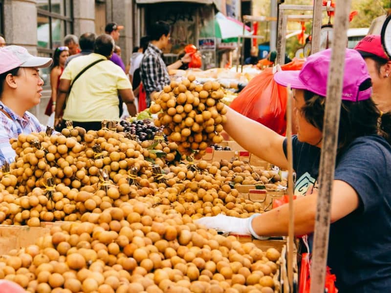 People shopping at a vibrant market in Chinatown, showcasing an array of longan fruit, highlighting the cultural and culinary diversity of the neighborhood.