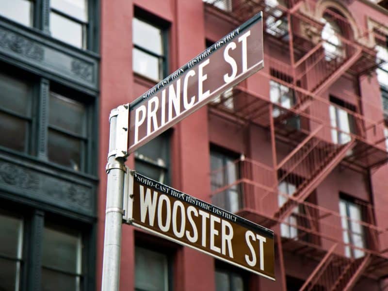 Street signs for Prince St and Wooster St in SoHo, showcasing the historic cast-iron architecture of the district.