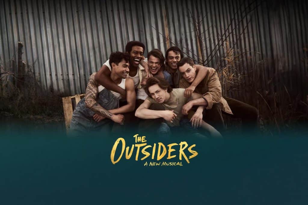 Group of young men portraying characters from "The Outsiders," a new musical, with a rustic backdrop reflecting the 1960s Tulsa setting.