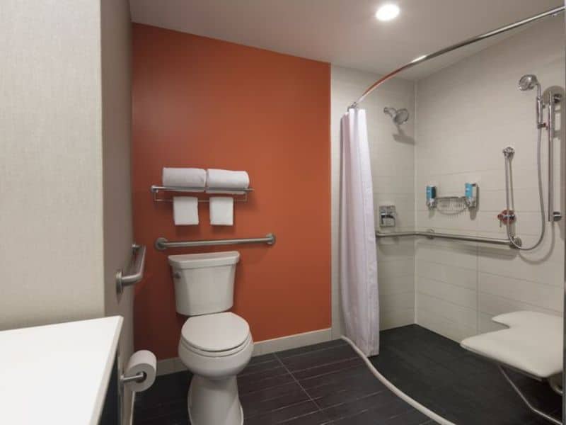 Accessible bathroom in Aloft Manhattan Downtown hotel featuring grab bars, shower with curtain, and modern fixtures.