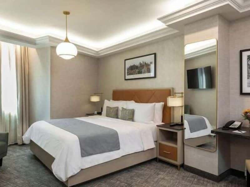 Elegant hotel room at Broadway Plaza Hotel featuring a king-size bed, contemporary decor, flat-screen TV, and modern amenities in the Nomad district of New York City.