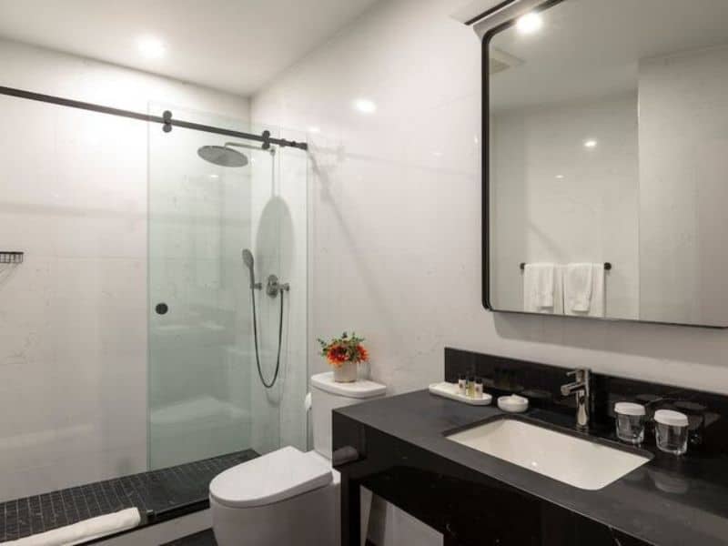 Modern hotel bathroom with walk-in shower, black countertop, and elegant decor, featuring a mirror, toiletries, and a small flower arrangement, reflecting the stylish amenities of Broadway Plaza Hotel in the Nomad district.
