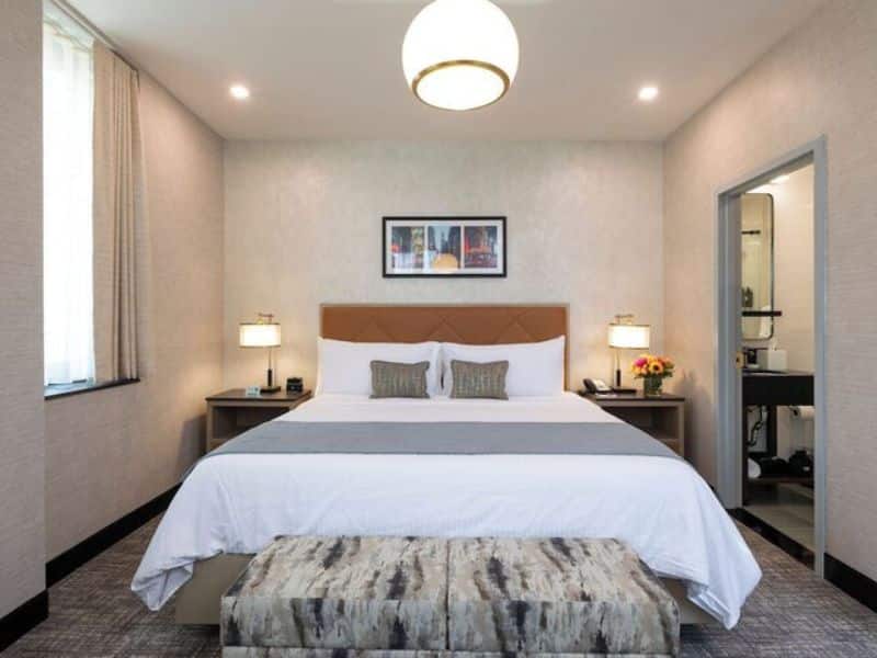 Elegant hotel room at Broadway Plaza Hotel, featuring a king-sized bed with decorative pillows, contemporary artwork on the wall, bedside lamps, and a cozy sitting area, showcasing modern design in the Nomad district of New York City.