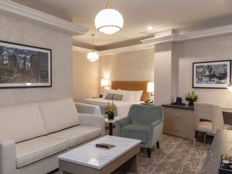 Elegant hotel room at Broadway Plaza Hotel, featuring a cozy sitting area with a sofa and armchair, contemporary art on the walls, a queen bed, and modern lighting, located in the vibrant Nomad district of New York City.