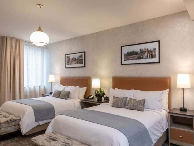 Elegant hotel room at Broadway Plaza Hotel featuring two beds, contemporary decor, soft lighting, and artwork on the walls, highlighting stylish accommodations in New York City's Nomad district.