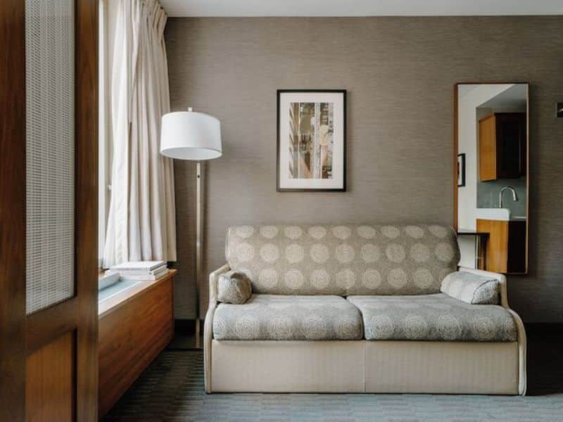 Cozy sitting area in a Club Quarters Hotel Grand Central room, featuring a patterned sofa, floor lamp, and artwork, highlighting elegant accommodations near Grand Central Station.