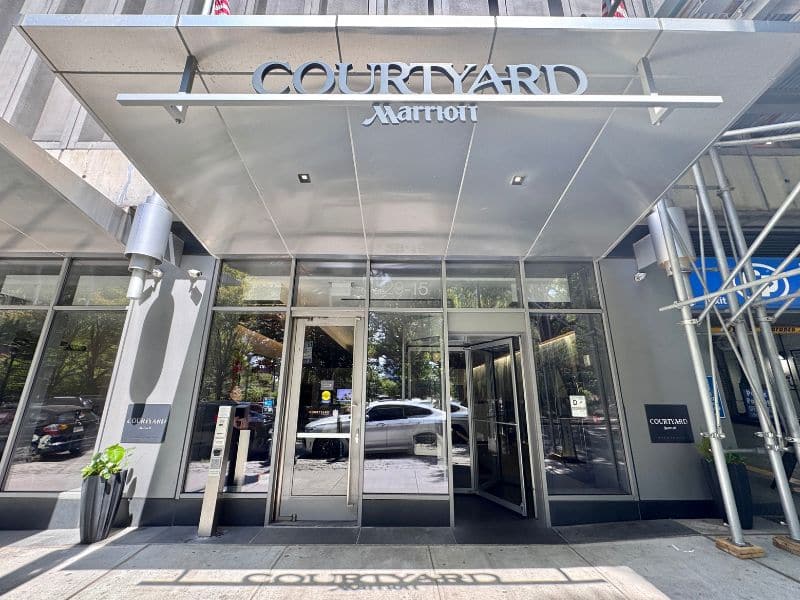 Courtyard by Marriott hotel entrance in Long Island City, featuring modern glass doors, a sleek sign, and surrounding urban landscape.