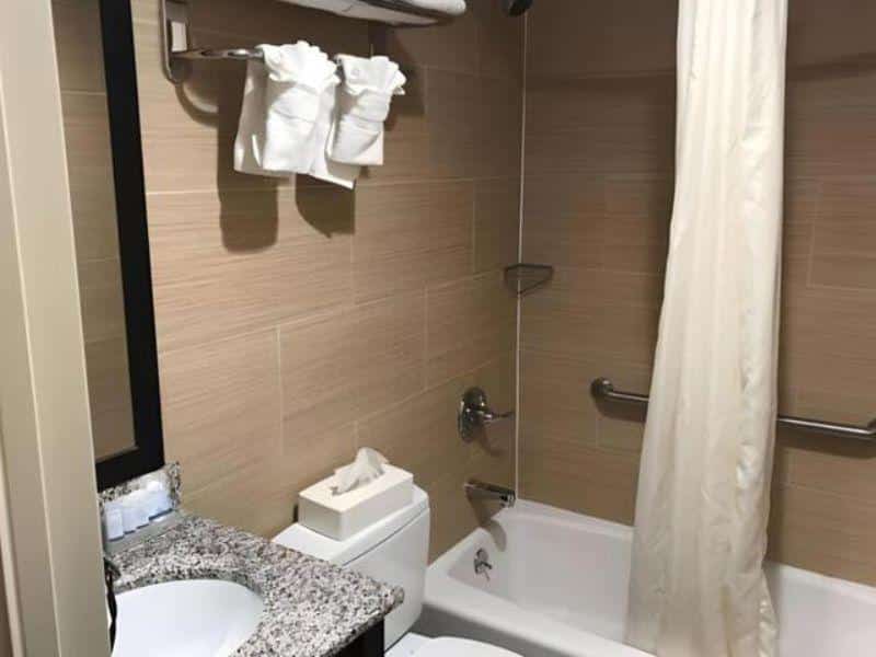 Bathroom in Days Inn by Wyndham Brooklyn Borough Park featuring a bathtub, shower curtain, sink with granite countertop, toiletries, and towels.