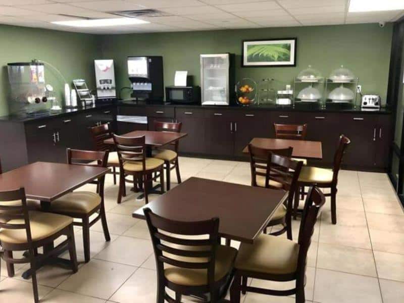 Breakfast area with tables and chairs, featuring a coffee station, microwave, and food display, at Days Inn by Wyndham Brooklyn Borough Park.