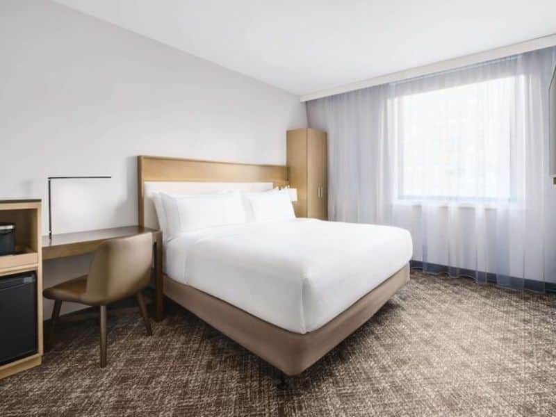 Cozy guest room at DoubleTree by Hilton New York Times Square South featuring a queen bed, desk area, and large window with natural light.
