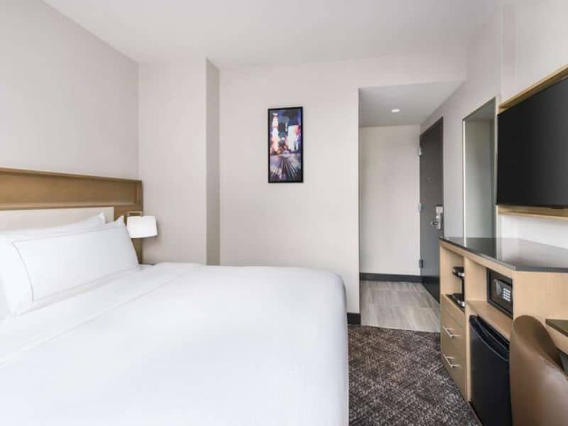 Cozy hotel room at DoubleTree by Hilton New York Times Square South featuring a king-size bed, modern decor, and amenities like a TV and mini-fridge, with a view of the vibrant Garment District.