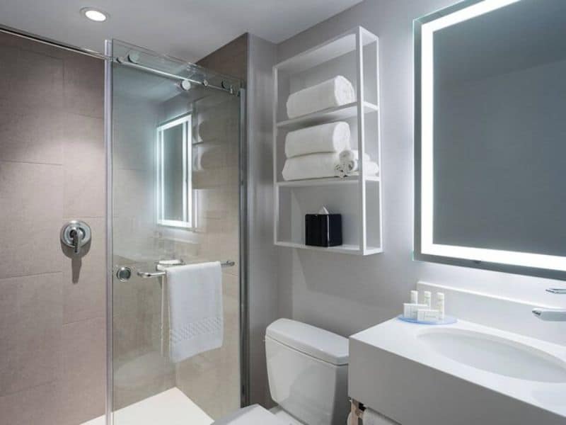 Modern hotel bathroom with glass shower, neatly arranged towels, illuminated mirror, and toiletries at Fairfield Inn & Suites by Marriott New York Manhattan/Central Park.
