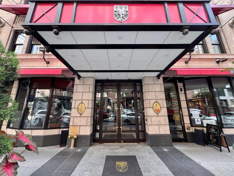 Fitzpatrick Manhattan hotel entrance with Irish-themed decor, featuring a red awning, glass doors, and stone facade, located in Midtown near Central Park and 5th Avenue shopping.