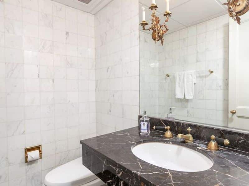 Modern bathroom with marble walls, dark marble countertop, sink, and vintage-style fixtures at Fitzpatrick Manhattan hotel.