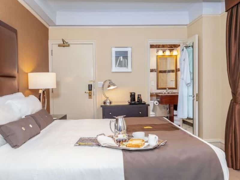 Cozy hotel room at Fitzpatrick Manhattan featuring a king-size bed with decorative pillows, a tray with breakfast items, modern furnishings, and an en-suite bathroom, emphasizing comfort and convenience for travelers.