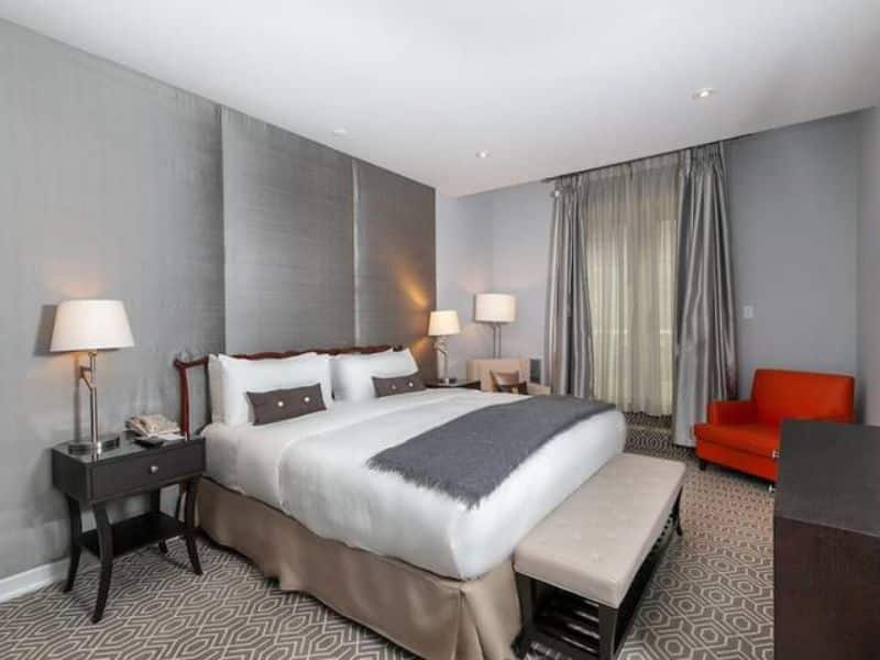 Modern hotel room at Fitzpatrick Manhattan featuring a king-sized bed, elegant decor, flat-screen TV, and cozy seating area with an orange chair, highlighting the hotel's Irish-themed ambiance and comfort.
