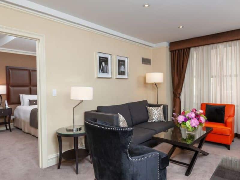 Modern suite at Fitzpatrick Manhattan hotel featuring a stylish living area with a black sofa, orange armchair, and floral centerpiece, showcasing the hotel's luxurious accommodations in Midtown New York City.