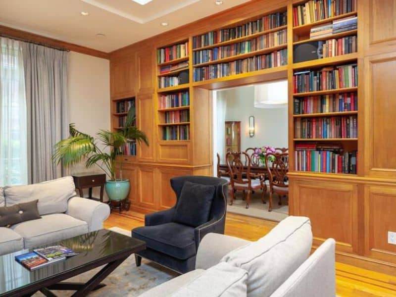 Cozy lounge area in Fitzpatrick Manhattan hotel featuring plush seating, a wooden bookshelf filled with colorful books, and a view into a dining area.