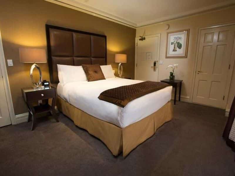 Modern hotel room at Fitzpatrick Manhattan featuring a queen bed with leather headboard, nightstands, and warm-toned decor, highlighting comfort and elegance in Midtown Manhattan.