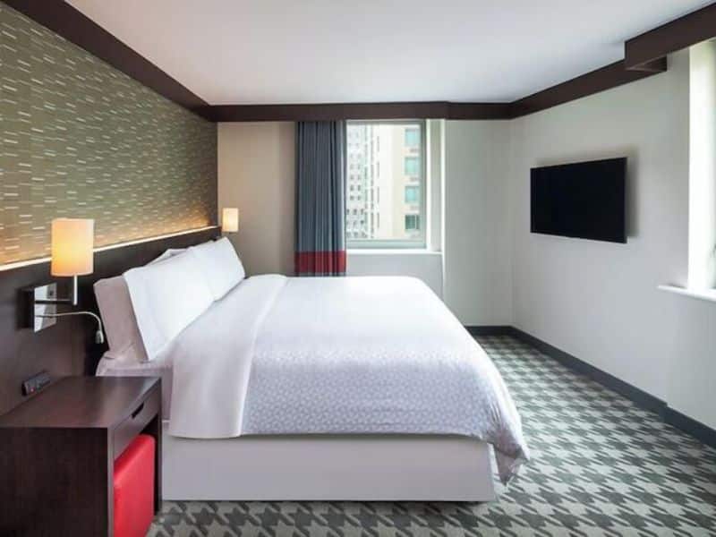 Modern hotel room at Four Points by Sheraton New York Downtown, featuring a king-size bed, flat-screen TV, and large windows with city views, highlighting contemporary design and comfort for business and leisure travelers.