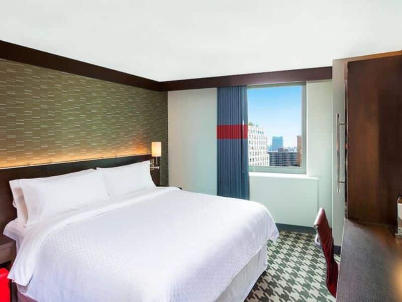 Modern hotel room at Four Points by Sheraton New York Downtown, featuring a queen bed, contemporary decor, large window with city view, and workspace with ergonomic chair.
