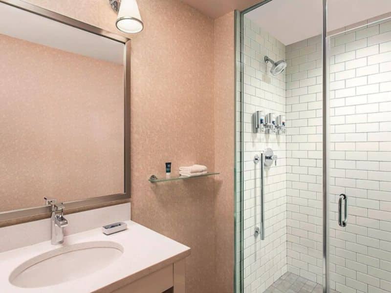 Modern hotel bathroom with a glass shower, white subway tiles, sink, and mirror, showcasing amenities at Four Points by Sheraton New York Downtown.