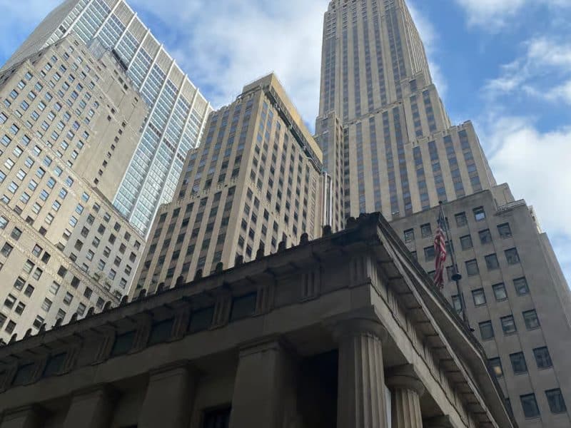 Historic architecture and iconic skyscrapers in Southern Manhattan, including the Woolworth Building, against a cloudy sky, illustrating the area's rich history and financial significance.