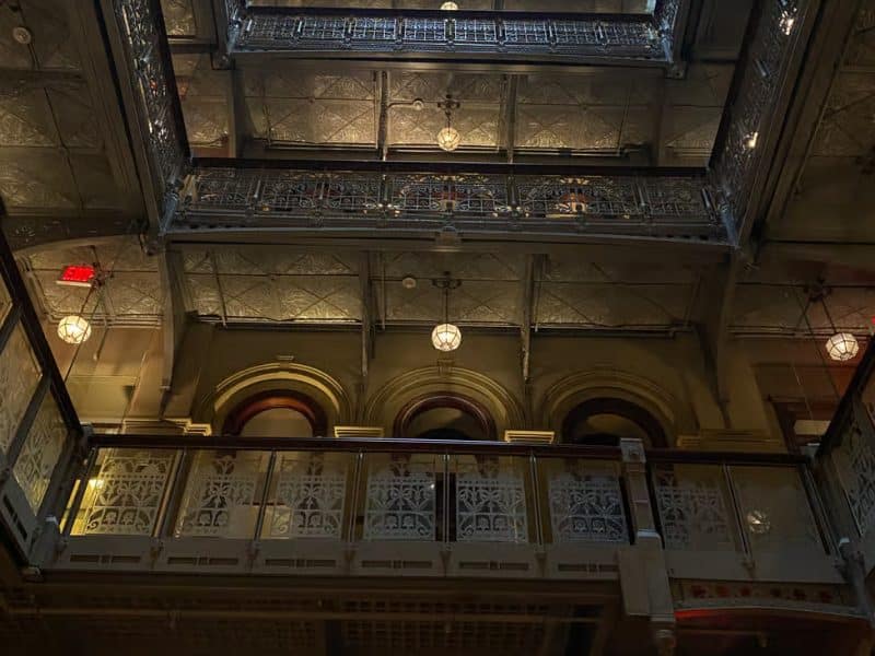 Interior view of a historic building in Southern Manhattan, showcasing ornate architectural details, intricate metalwork, and vintage light fixtures, reflecting the area's rich history and cultural significance.