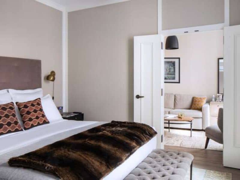 Cozy hotel room at HGU New York with a plush bed, decorative pillows, and a view of a sitting area through an open door, highlighting the boutique hotel's luxurious amenities.